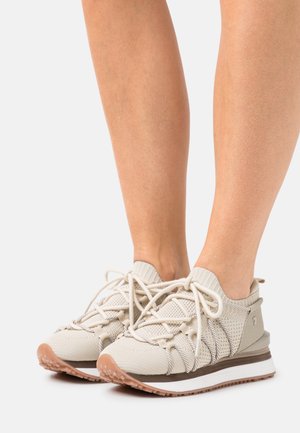 Light beige athletic shoes with a knitted upper, elastic laces, textured sides, and rubber outsole for traction. Low profile design.