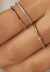Drei goldene Ringe an einer Hand: einer glatt, einer mit kleinen funkelnden Steinen und einer mit einem einzelnen Edelsteinakzent.