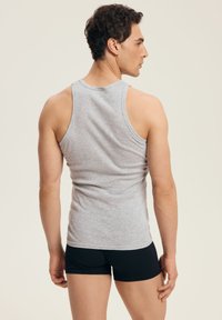 Szary bawełniany top na ramiączkach o dopasowanym kroju i szerokich ramiączkach, zestawiony z czarnymi szortami, pokazany od tyłu na jasnym tle.