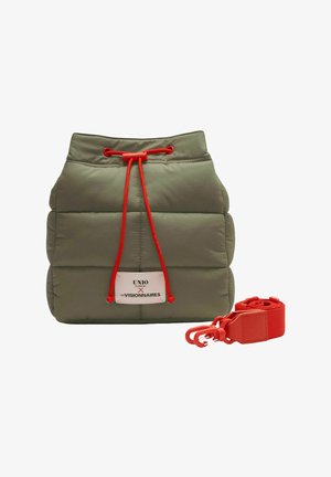 Pochette matelassée vert olive avec cordon de serrage rouge et bandoulière détachable rouge, équipée d'une étiquette blanche avec texte noir et rouge.
