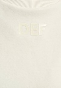 Hvid strikket sweater med høj hals og prægede "DEF" logo i en lidt lysere nuance. Blød tekstur og minimalistisk design.