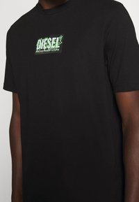 Černé tričko s krátkým rukávem se svěžím a barevným grafickým logem "DIESEL" v zelené barvě, vyrobené z hladkého bavlněného materiálu.