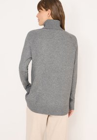 Pull en maille gris avec un col haut en côtes, des manches raglan et une coupe décontractée. Il présente des poignets à côtes et un ourlet inférieur, avec une texture douce.