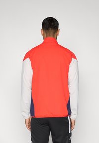 Κόκκινο και άσπρο μπουφάν με επένδυση αέρα, με ψηλό γιακά και αντίθετες ναυτικές λεπτομέρειες. Διαθέτει ελαστικές μανσέτες και χαλαρή εφαρμογή.