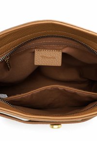 Interno di una borsa in pelle color cuoio con una texture liscia, dotata di una tasca con cerniera e di un'etichetta con logo. Dettagli cuciti lungo il bordo superiore.