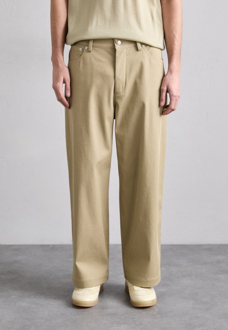 Beige bomullsshorts med avslappnad passform, utrustade med dragkedja, framfickor och en mjuk yta. Bärs med krämfärgade skor.