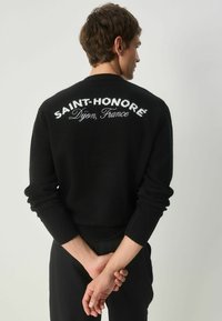 Sort striktrøje med hvid broderet tekst "SAINT-HONORÉ Dijon, Frankrig" på ryggen. Ribbet manchetter og kant.