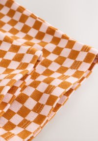 Tissu à carreaux orange et rose avec une texture douce, plié, présentant des coutures blanches le long des bords et un motif à carreaux distinct.