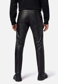 Schwarze Lederhosen mit einer figurbetonten Passform, ausgestattet mit zwei Gesäßtaschen und einer glatten Textur, kombiniert mit schwarzen Schuhen.