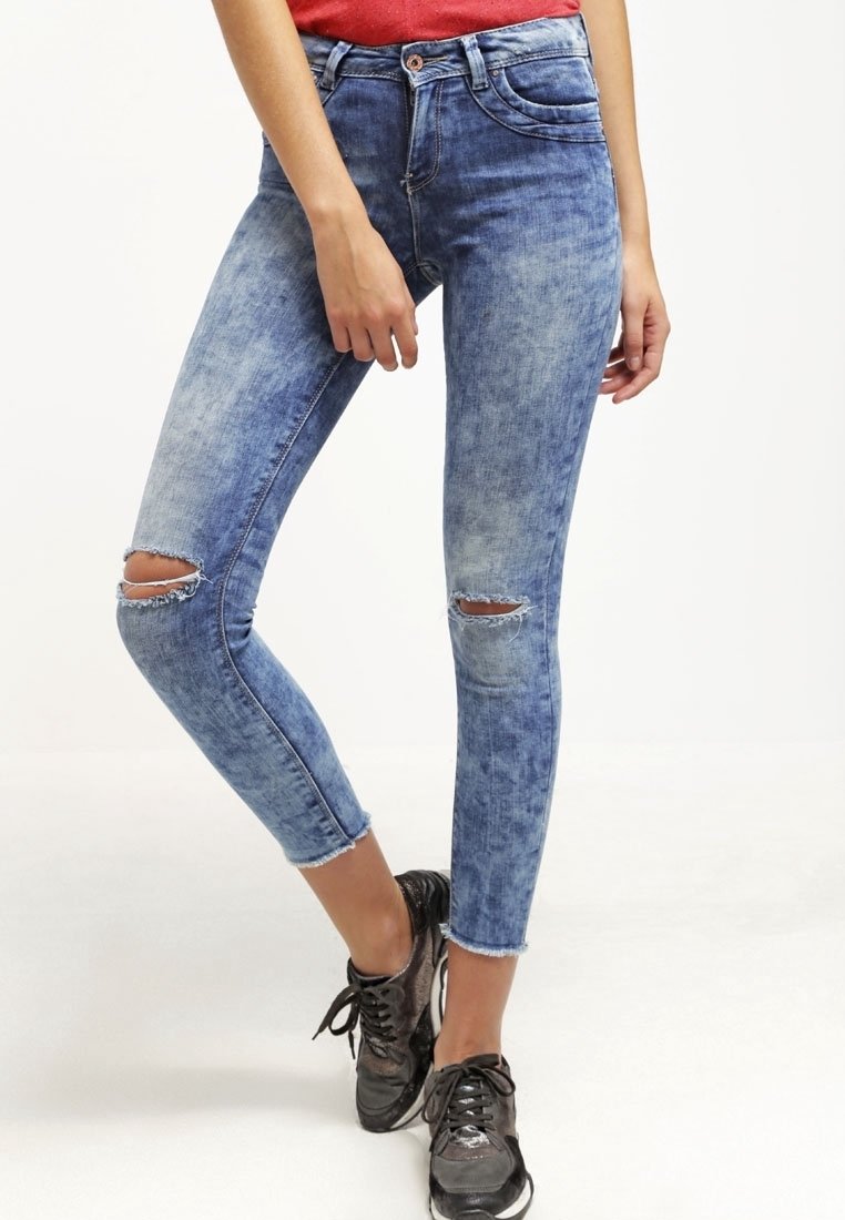 Úzké džíny vyrobené z světle modrého denimu, s potrhanými otvory na kolenou, bledým povrchem a roztrhanými detaily na lemu.
