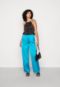 Top halter preto com decote franzido, combinado com calças largas brilhantes em turquesa. Acessórios incluem uma pequena bolsa preta e sandálias de salto.