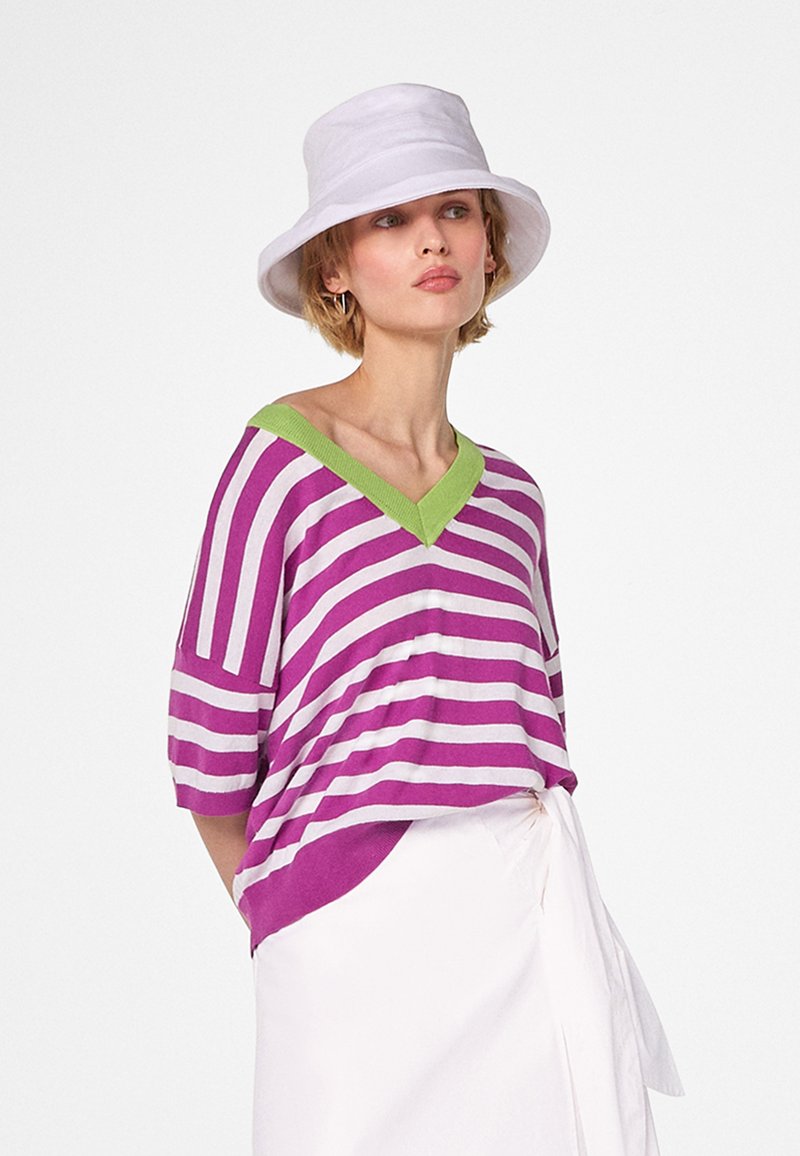 Purple and white striped short-sleeve v-neck sweater with green trim, paired with a white bucket hat and white wrap skirt.