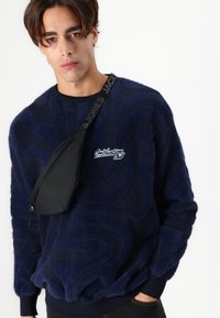 Mørkeblå fleece sweatshirt med tekstureret bølgende mønster, ribbede manchetter og et broderet logo. Sæt sammen med en slank sort skuldertaske.