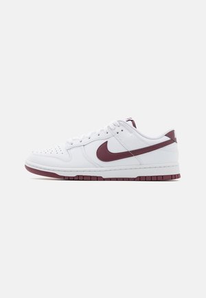 Biały niski sneaker z bordowym logo Nike swoosh i pasującymi bordowymi akcentami na podeszwie, widoczny z boku na jednolitym tle.