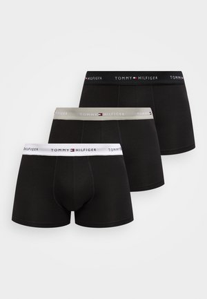 Trois boxers noirs Tommy Hilfiger avec des ceintures de marque blanches, grises et noires, disposés en chevauchement sur un fond blanc.