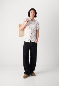 Short-sleeve white shirt with small blue patterns, paired with dark wide-leg jeans and light brown shoes, holding a beige tote bag.