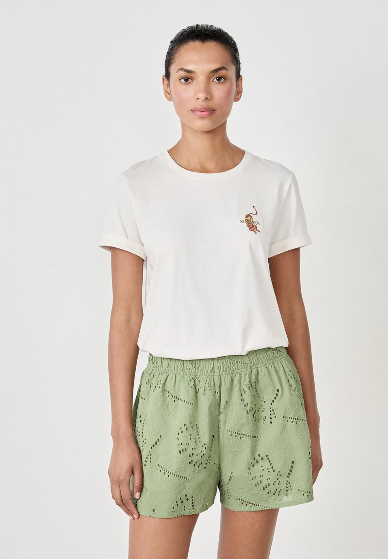 Camiseta blanca de algodón con mangas arrolladas y diseño bordado de "Verano". Pantalones cortos verdes con cortes de encaje y cintura elástica.