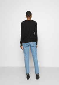 Svart långärmad tröja i avslappnad passform, kombinerad med ljusblå raka jeans med fransar i nederkant och svarta ankelskor.