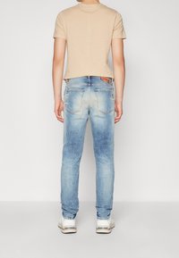 Beige lyhythihainen paita yhdistettynä vaaleansinisiin, kuluneisiin skinny-farkkuihin, joissa on takataskut ja merkkilogo, käytetty vaaleiden lenkkitossujen kanssa.