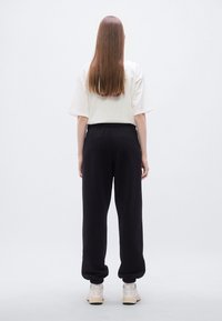 Μαύρο παντελόνι φόρμας με ελαστική μέση, μανσέτες στα πόδια και άνετη εφαρμογή, συνδυασμένο με ανοιχτόχρωμο κοντομάνικο τοπ.