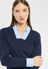 Marineblauwe pullover met een V-vormige halslijn, voorzien van een lichtblauwe en witte gestreepte kraag en manchetten. Soepele textuur, lange mouwen.