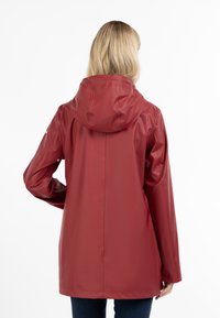 Giacca impermeabile rossa con cappuccio, maniche lunghe e taglio dritto. Tessuto liscio con minima ferramenta e senza accenti evidenti.