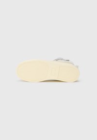 Witte sneaker met een gestructureerde rubberen zool, beige accenten en een gladde bovenkant. Beschikt over aanpasbare veters en subtiele branding aan de zijkant.