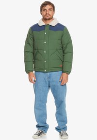 Grøn polstret jakke med en marineblå skuldre og faux shearling krave. Har trykknaplukning, to frontlommer og et kvadratisk snit.