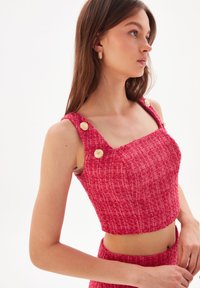 Cropped top rosa brillante realizzato in tessuto texture, con scollatura quadrata e grandi bottoni dorati sulle spalline.