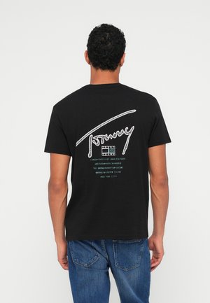 Melna kokvilnas t-krekls ar lielu baltu paraksta logotipu uz muguras, zem kura ir nospiesti pilsētu nosaukumi tīrkārtā krāsā. Īsas piedurknes, apaļa kakla izgriezums.