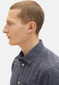 Mörkblå herrskjorta med krage, som har en texturerad tyg, knappstängning och en bröstficka. Skjortan har ett subtilt mönster och en klassisk design.