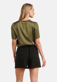 Olijfgroene satijnen blouse met korte pofmouwen en een gerimpelde kraag, gecombineerd met zwarte shorts met elastische taille, zachte textuur, casual pasvorm.