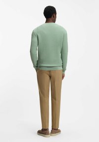 Vaaleanvihreä, pintakuviollinen neulepaita, pyöreä pääntie, resorit hihansuissa, yhdistetty hiekanvärisiin housuihin ja ruskeisiin nyörikenkiin. Asun takaosa.