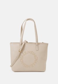 Beige läderväska med dubbla handtag, justerbar axelrem och cirkulär logotypdetalj prydd med nitar på framsidan.