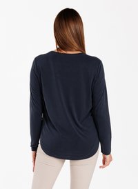 Langärmliges marineblaues Hemd aus weichem Stoff, mit rundem Halsausschnitt und einem längeren hinteren Saum, kombiniert mit hellbeigen Hosen.
