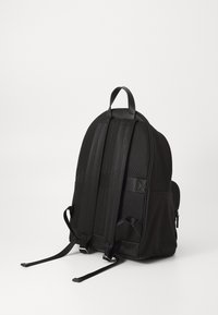 Mochila negra con un exterior liso, correas acolchadas y acentos de malla. Cuenta con correas ajustables duales y un asa en la parte superior para llevar.