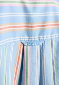 Material cu dungi orizontale și verticale pastelate în albastru, verde, roz și bej, având o pliură cusută și eticheta brandului Pleat and Joules.