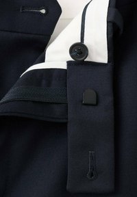 Tkanina marynarki w kolorze granatowym z białym obszyciem kołnierza. Zawiera czarny guzik i czarny rzep. Gładka tekstura i dopasowany krój.