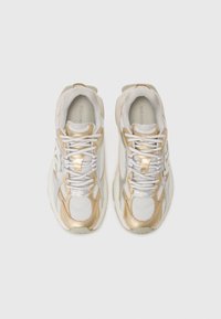 White athletic shoes with gold metallic accents, mesh panels, and round rubber soles. Features laces and padded collar for comfort.