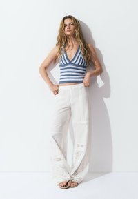Top de ganchillo con rayas azules y blancas, combinado con pantalones sueltos blancos con estampado y detalles de encaje, acompañado de sandalias planas.