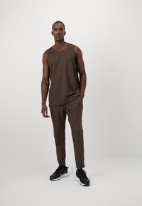 Un débardeur brun sans manches associé à un pantalon brun ajusté assorti. Présente une texture douce et un design minimaliste. Porté avec des baskets noires.