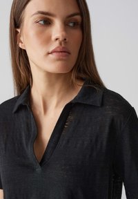 Top nero a maniche corte in tessuto leggero e testurizzato. Presenta una scollatura a V e una vestibilità ampia, enfatizzando un design rilassato.