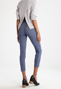 Gray textured sweater with a split back, paired with blue patterned trousers and black heeled shoes. Trousers are cropped at the ankle.