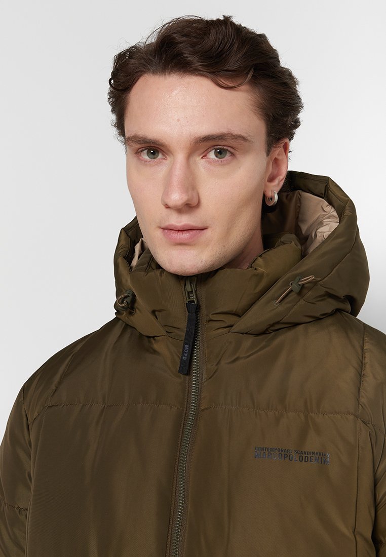 Olivgrüne Steppjacke mit hohem Kragen, Reißverschluss vorne und verstellbarem Kapuze. Strukturstoff zeigt ein gestepptes Design. Branding auf der Brust.