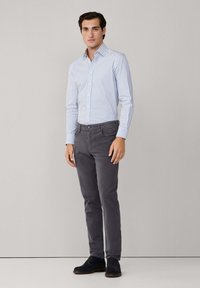 Camisa de cuadros blanca y azul claro, pantalones gris ajustados y zapatos de ante azul oscuro. Texturas suaves con un corte a medida.