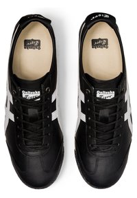 Mustat nahkasneakersit, joissa on valkoiset raidat, teksturoitu pinta, litteät nauhat ja beige sisäpohja, jossa on "Onitsuka Tiger" -brändäys.