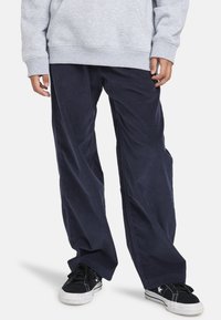 Marineblå corduroy bukser med brede ben, struktureret stof og sidelommer, parret med sorte sneakers med kontrastsyninger.