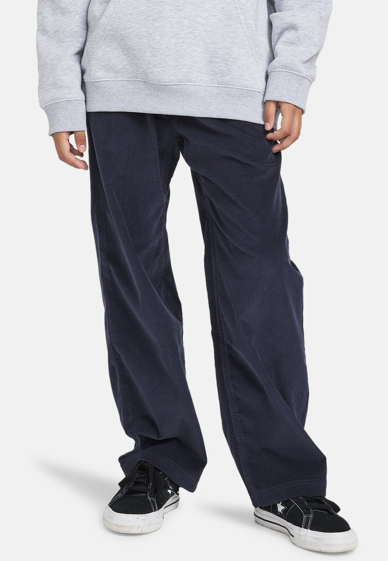 Marineblå corduroy bukser med brede ben, struktureret stof og sidelommer, parret med sorte sneakers med kontrastsyninger.