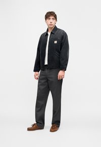 Μαύρο τζιν μπουφάν με φερμουάρ μπροστά, τσέπη με επιθετικό σχέδιο, συνδυασμένο με γκρι παντελόνια και καφέ παπούτσια. Απλός, ευθύγραμμος σχεδιασμός.