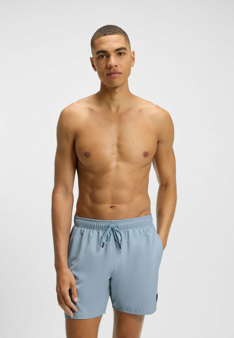 Pantaloncini da bagno azzurri chiari realizzati in un materiale liscio, con vita elastica, cordoncino regolabile e un piccolo logo di lato.